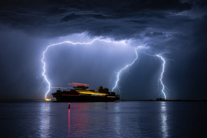 3 lightening strikes in the sky illuminating a large ship in the sea