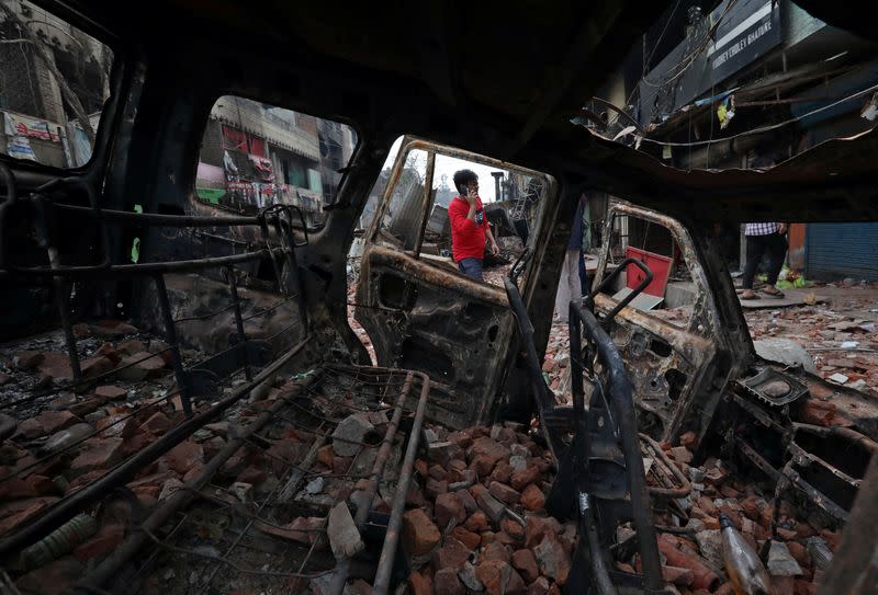 A man speaking on a mobile phone is seen through a burnt vehicle in a riot affected area following clashes between people demonstrating for and against a new citizenship law in New Delhi