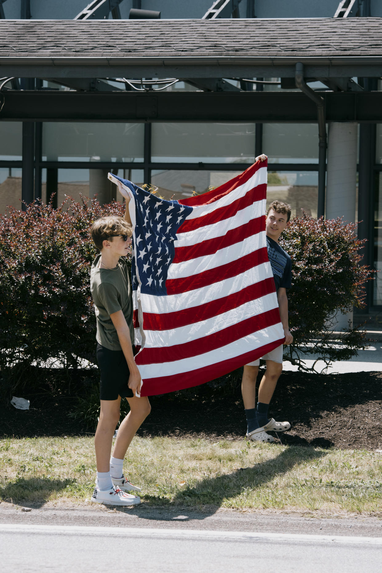 People hold an American flag in preparation for the passing of the funeral procession for Corey Comperatore, who was killed during the shooting at former President Donald Trump’s rally last Saturday, in Cabot, Pa., on Friday, July 19, 2024. (Kristian Thacker/The New York Times)