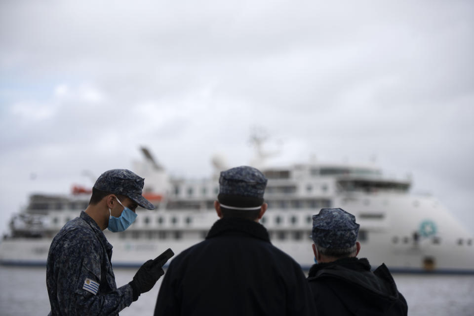 Members of the Uruguayan military wait for passengers to disembark from the Australian cruise ship "Greg Mortimer" in order to transport them to the international airport, in Montevideo, Uruguay, Wednesday, April 15, 2020. The ship has been anchored off Uruguay's coast since March 27 with more than half its passengers and crew infected with the new coronavirus, according to authorities. (AP Photo/Matilde Campodonico)
