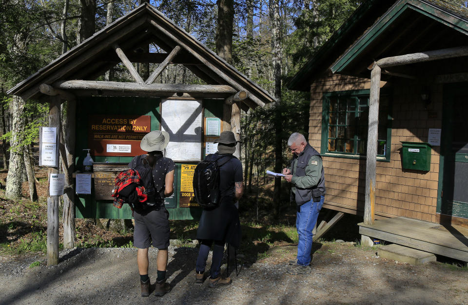 Adirondack Mountain Reserve Ranger Mike Ryan, right, checks in two hikers at the trailhead of the reserve, Saturday, May 15, 202, in St. Huberts, N.Y. A free reservation system went online recently to control the growing number of visitors packing the parking lot and tramping on the trails through the private land of the Adirondack Mountain Reserve. The increasingly common requirements, in effect from Maui to Maine, offer a trade-off to visitors, sacrificing spontaneity and ease of access for benefits like guaranteed parking spots and more elbow room in the woods. (AP Photo/Julie Jacobson)