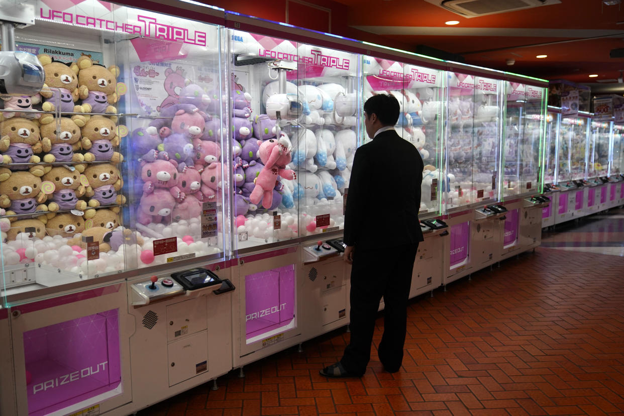 A man wearing a suit watches as a doll he grabbed with the machine's claw is dropped back into the box while playing a crane game Wednesday, Sept. 11, 2019, in the Akihabara district of Tokyo. (AP Photo/Jae C. Hong)