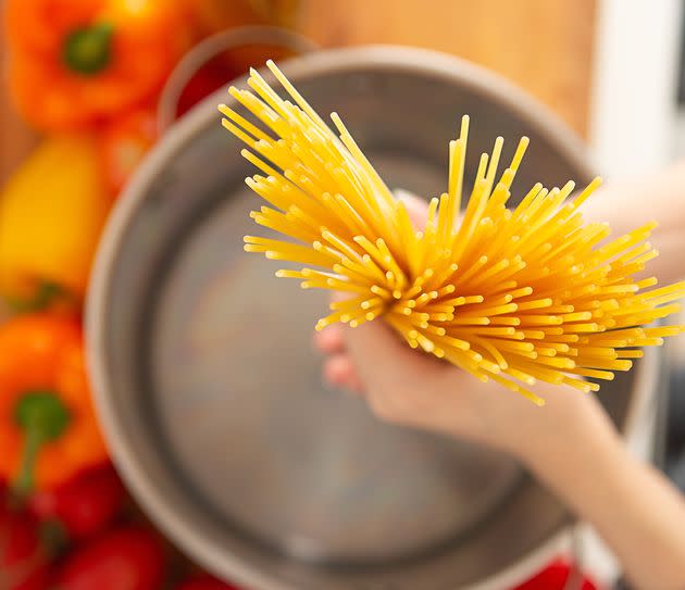 Above view of hand holding a handful of raw pasta noodle in pot in kitchen (Photo: ChristopherBernard via Getty Images)