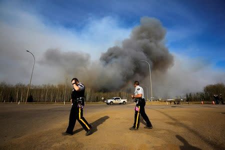 RCMP police officers stand in front of smoke from the the wildfires near Fort McMurray, Alberta, Canada, May 6, 2016. REUTERS/Mark Blinch