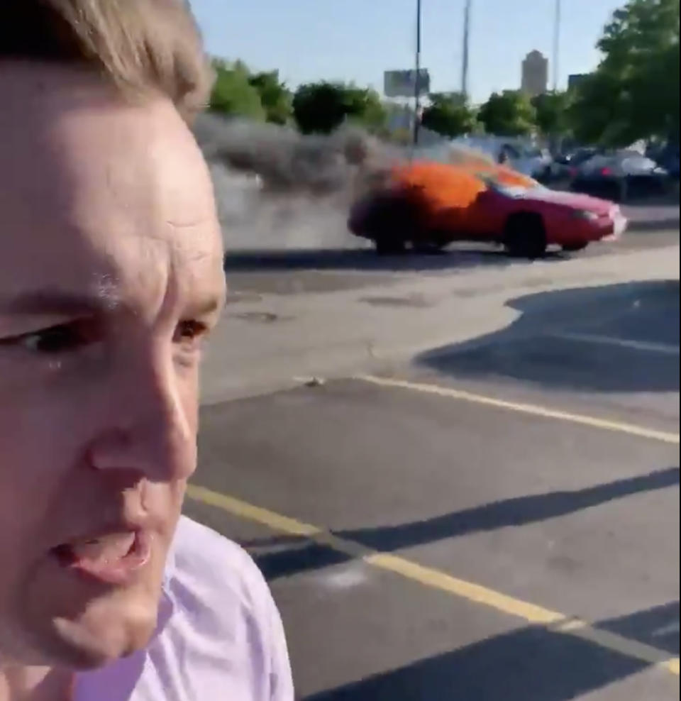 Tim Arvier stands in front of a car on fire in Minneapolis.