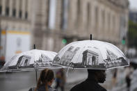 People with umbrellas depicting Paris landmarks walk down a road along the Seine River, reopened to pedestrians following Friday's opening ceremony, at the 2024 Summer Olympics, Saturday, July 27, 2024, in Paris, France. (AP Photo/Rebecca Blackwell)