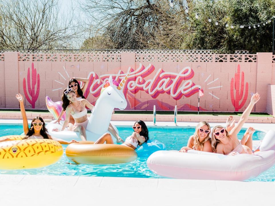 A group of woman lounge in a pool on colorful floaties.