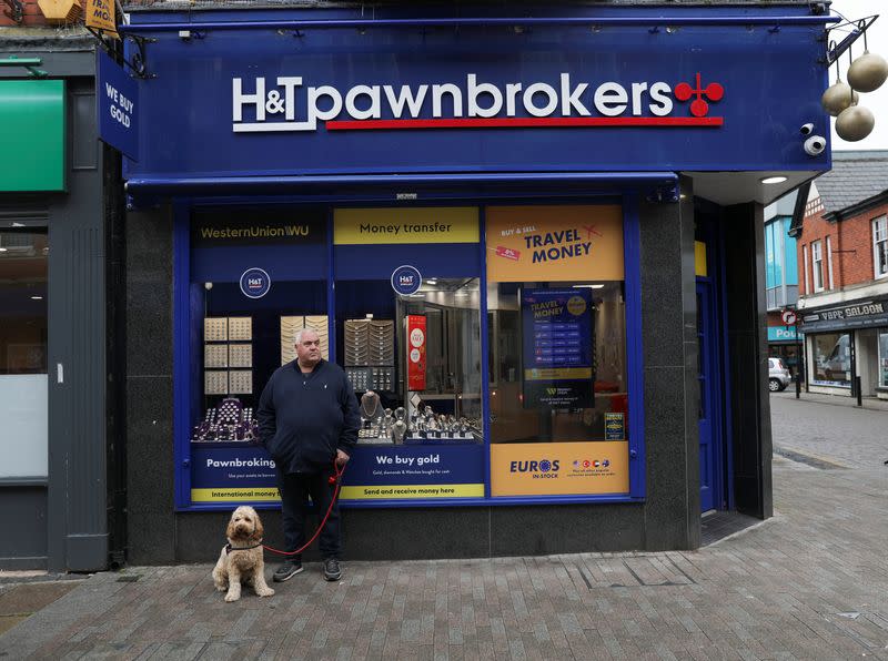 A man stands with his dog in front of a currency exchange and pawn shop in Leigh