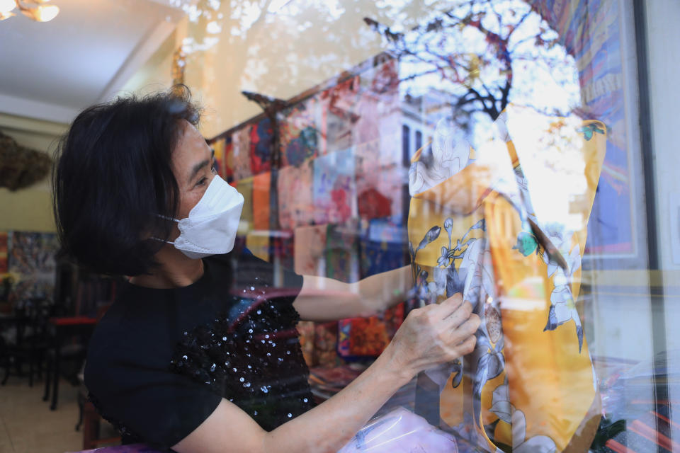 A shop owner arranges silk products for the shop window display in the old quarter of Hanoi, Vietnam on Wednesday, March 16, 2022. Vietnam on Wednesday scrapped quarantine and other travel restrictions for foreign visitors in an effort to fully reopen its border after two years of pandemic-related closure, the government said. (AP Photo/Hau Dinh)