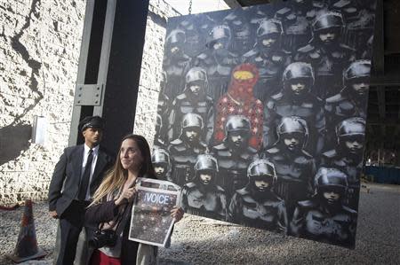 A woman poses for a photo in front of a new art installation by British graffiti artist Banksy in New York October 18, 2013. REUTERS/Carlo Allegri