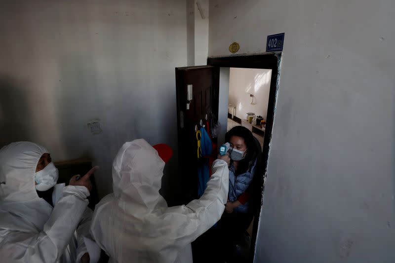 Worker in protective suit measures the body temperature of a woman during a door-to-door search to inspect residents following an outbreak of the novel coronavirus in Wuhan