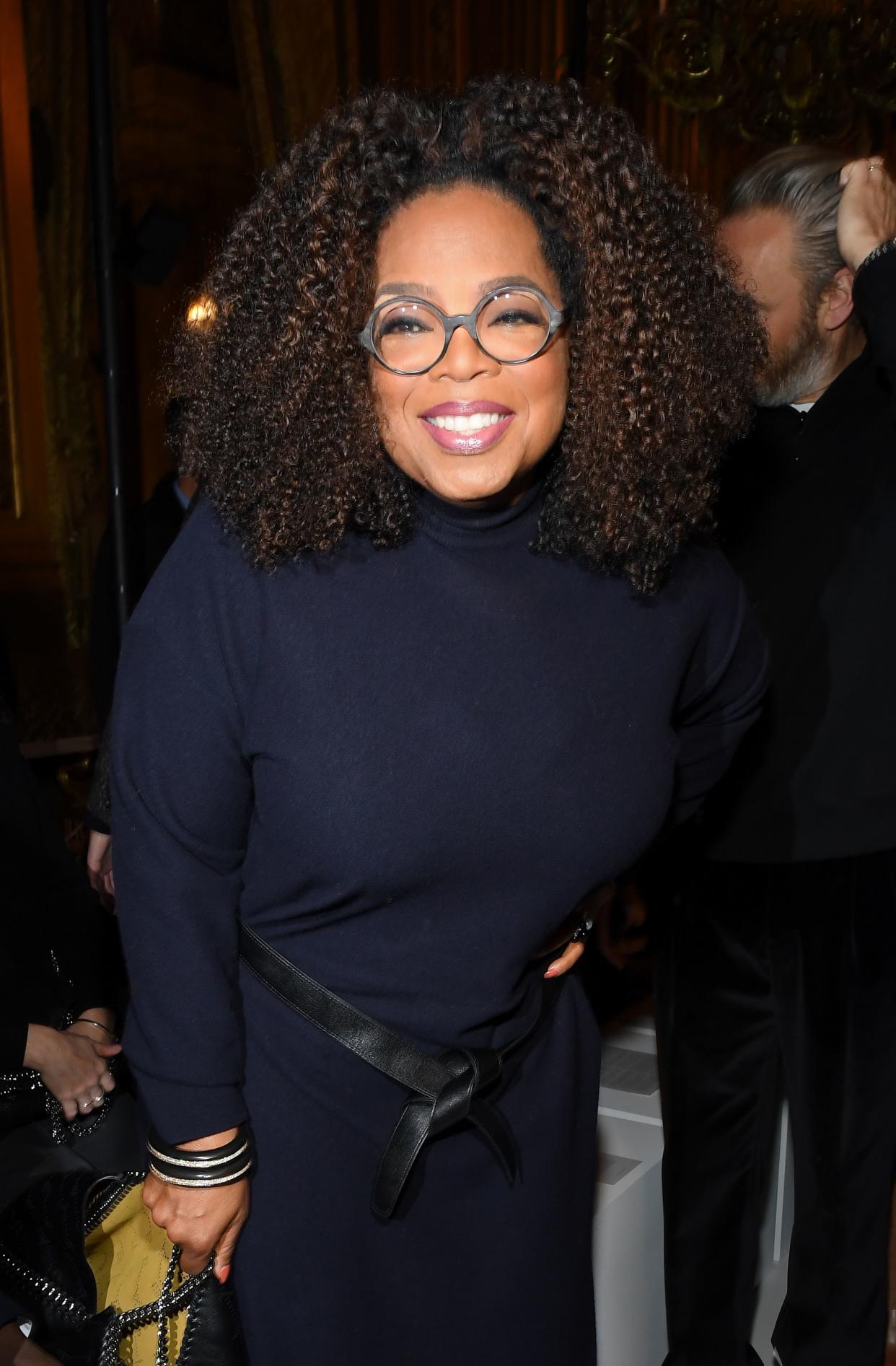 Oprah Winfrey poses beautifully for the camera in dark blue dress with a black stylish belt across her stomach.