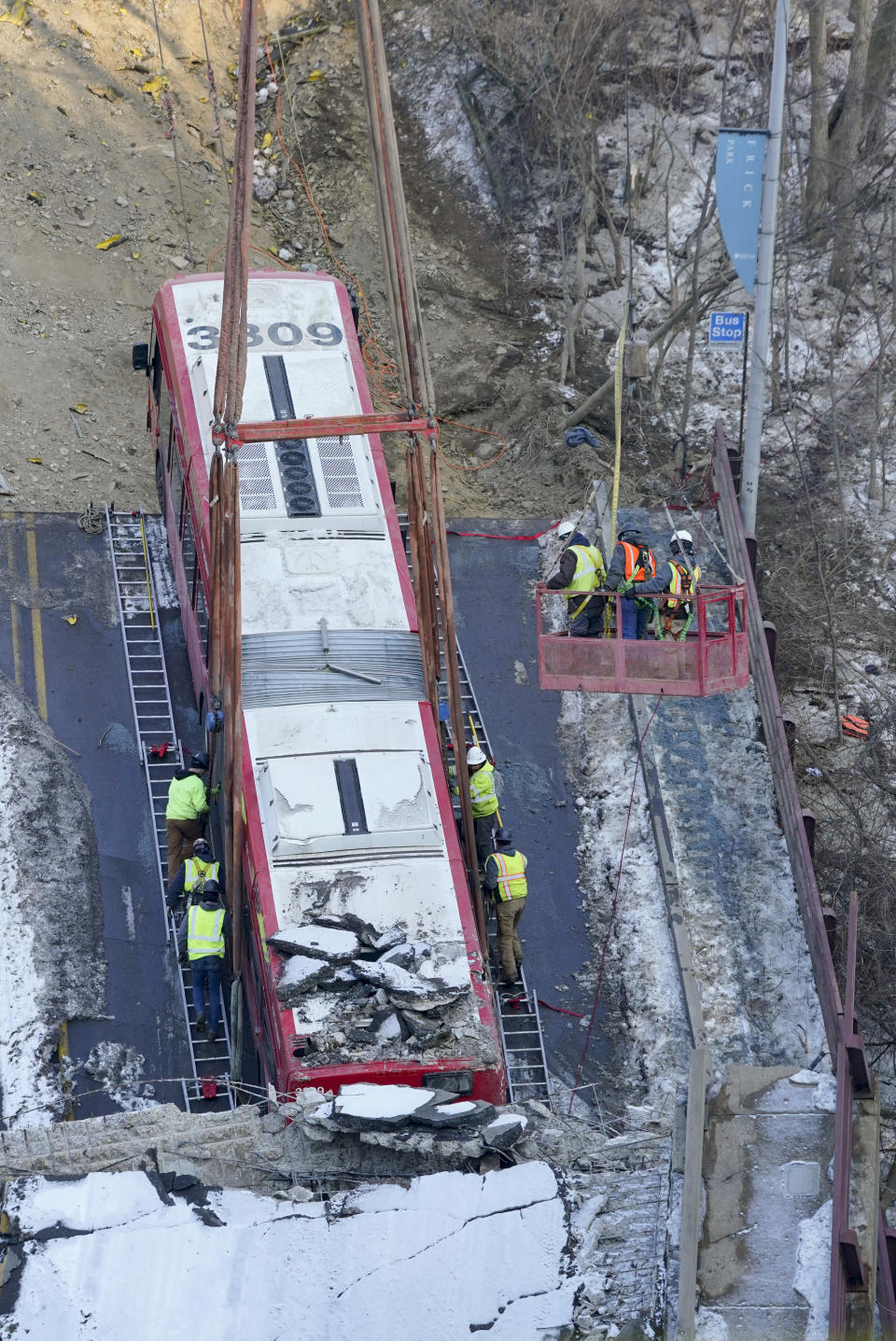 Some workers use ladders placed along the sides of the bus that was on a bridge when it collapsed Friday as they position the lifting apparatus to remove it as others in a crane suspended basket help position the mechanisms during the recovery process on Monday Jan. 31, 2022 in Pittsburgh's East End. (AP Photo/Gene J. Puskar)
