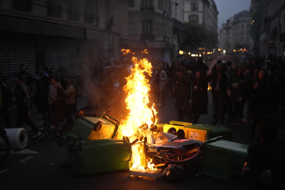 Protesters march behind burning garbage cans as they demonstrate after French President Emmanuel Macron tried to diffuse tensions in a televised address to the nation, Monday, April 17, 2023 in Paris. Emmanuel Macron said Monday that he heard people's anger over raising the retirement age from 62 to 64, but insisted that it was needed. (AP Photo/Thibault Camus)