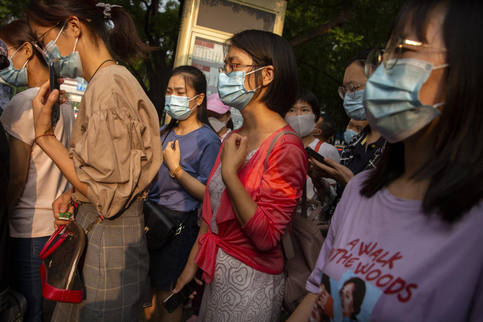 People wearing face masks to protect against the coronavirus wait at a bus stop in Beijing, Friday, July 31, 2020. China is tightening travel restrictions in the capital of Xinjiang, where more than a hundred new cases were reported Friday. (AP Photo/Mark Schiefelbein)