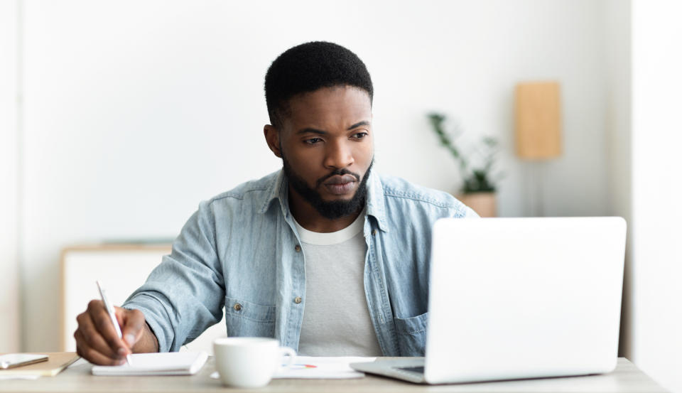 Job search. Unemployed man using laptop searching for vacancies online in internet and taking notes, panorama with copy space