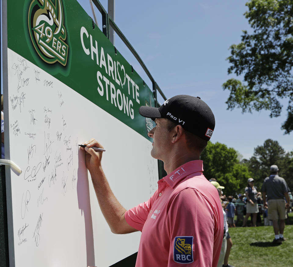 Webb Simpson signs a board on the first tee in support of the victims of the shooting at the University of North Carolina-Charlotte during the first round of the Wells Fargo Championship golf tournament at Quail Hollow Club in Charlotte, N.C., Thursday, May 2, 2019. (AP Photo/Chuck Burton)