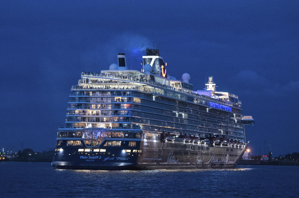 Passengers stand on board the Tui cruise ship 'Mein Schiff 2' during the departure from the port for a three-day trip on the North Sea in Hamburg, Germany, Friday, July 24, 2020. The cruise ship has set sail for the first time since the industry was shut down due to the coronavirus pandemic, with strict precautions to keep passengers and crew as safe as possible. Passengers will spend the weekend at sea with no land stops before returning to Germany on Monday. (Daniel Bockwoldt/dpa via AP)