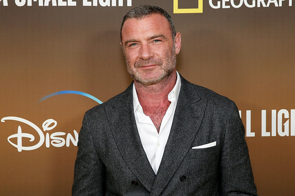 Mid-shot of actor Liev Schreiber as he smiles facing the camera.