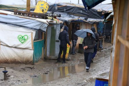 Migrants walk in the mud in the southern part of a camp for migrants called the "jungle", on a rainy winter day in Calais, northern France, February 22, 2016. REUTERS/Pascal Rossignol