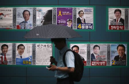 A man using his phone walks past election posters in Seoul June 2, 2014. REUTERS/Kim Hong-Ji