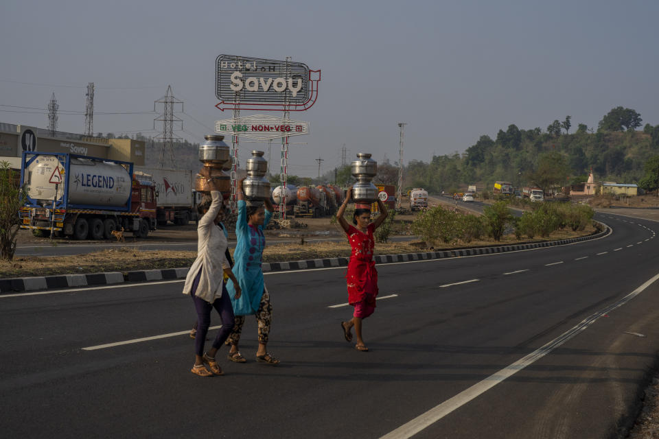 Women cross a highway after collecting water for cleaning and washing from a pit near Shahapur, northeast of Mumbai, India, Saturday, May 6, 2023. This is a common site across the rural Thane District, where water scarcity is a growing concern. (AP Photo/Dar Yasin)