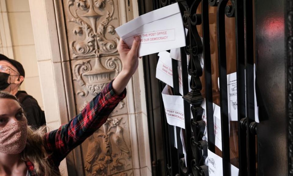 Demonstrators insert leaflets designed to look like mail-in ballots in the door of Louis DeJoy’s home in Washington DC.