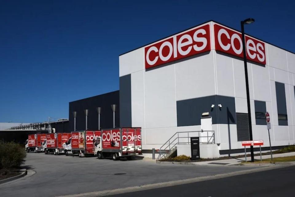 Coles delivery trucks line up outside supermarket warehouse.