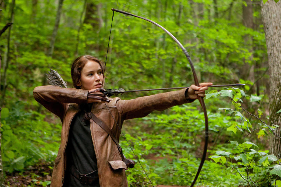 a woman aims a bow and arrow at something off screen