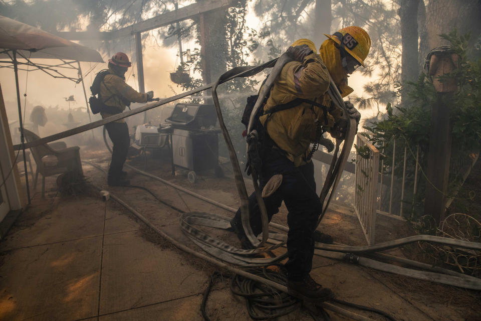 Firefighters pull hoses and spray flames behind a home in the Pacific Palisades area of Los Angeles, Oct. 21, 2019. (AP Photo/Christian Monterrosa)