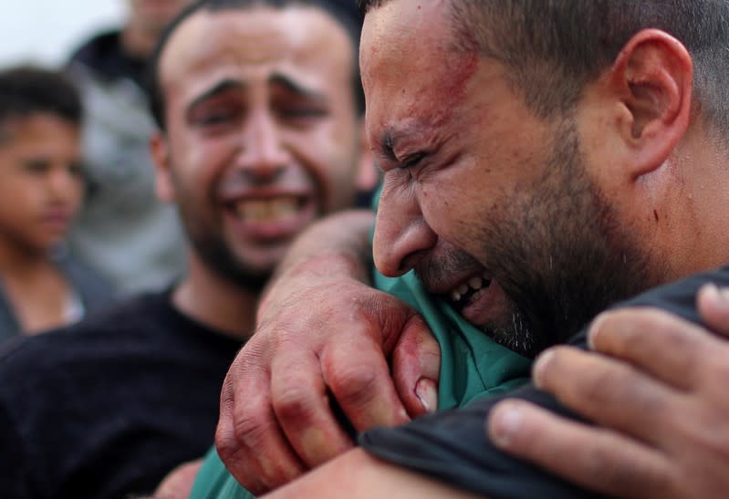 Palestinian man, stained with the blood of his relative, is comforted as he reacts at Shifa hospital in Gaza City