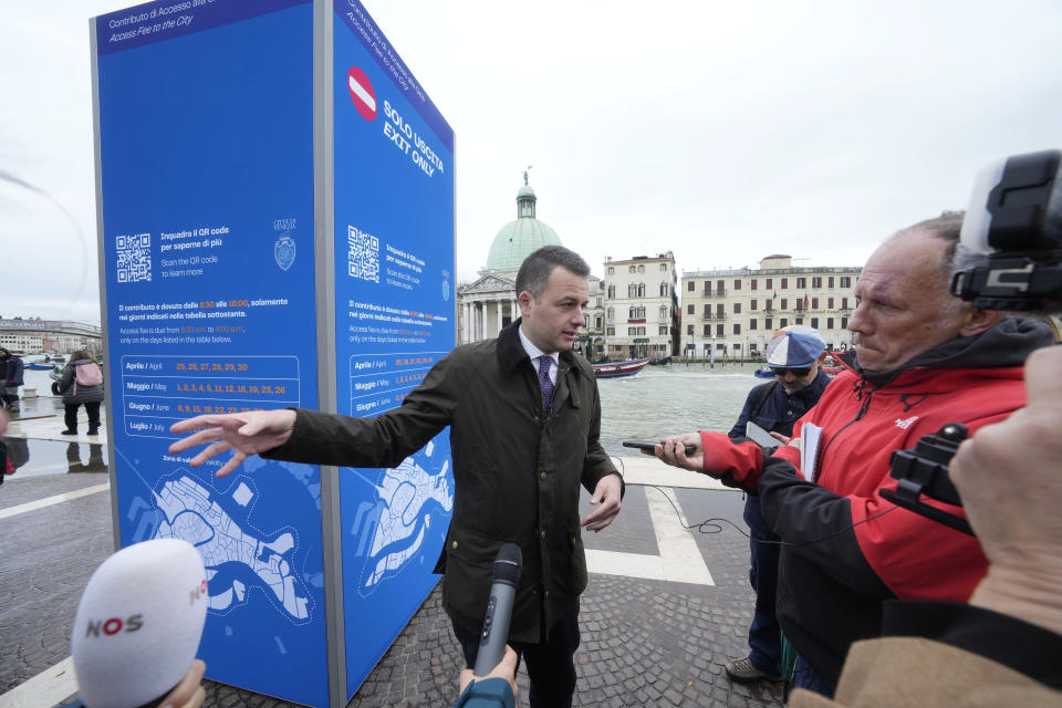 Venice councillor Simone Venturini speaks with reporters in front of a tourist tax totem in Venice, Italy, Wednesday, April 24, 2024. The lagoon city of Venice begins a pilot program Thursday, April 25, 2024 to charge daytrippers a 5 euro entry fee that authorities hope will discourage tourists from arriving on peak days. Officials expect some 10,000 people will pay the fee to access the city on the first day, downloading a QR code to prove their payment. (AP Photo/Luca Bruno)