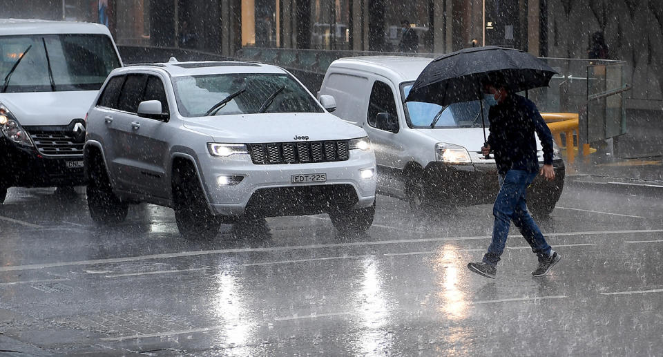 Man crossing a road with an umbrella in storm weather in Sydney.