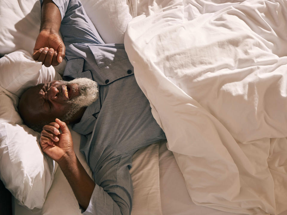 A mature man rouses in the early morning light, stretching as he wakes.