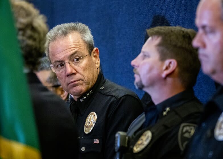 A police officer on the left looks over to others while standing next to each other, wearing black uniforms.