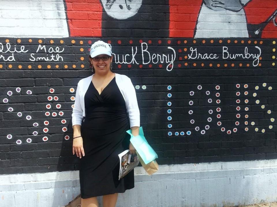 Carmen in front of black sign and mural that says "st Louis"