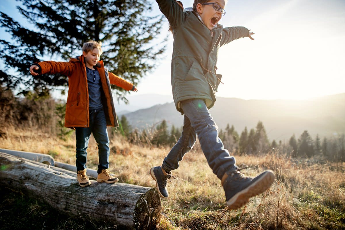 Two boys use a tree trunk as a balance beam as the walk through a forest while hiking. 