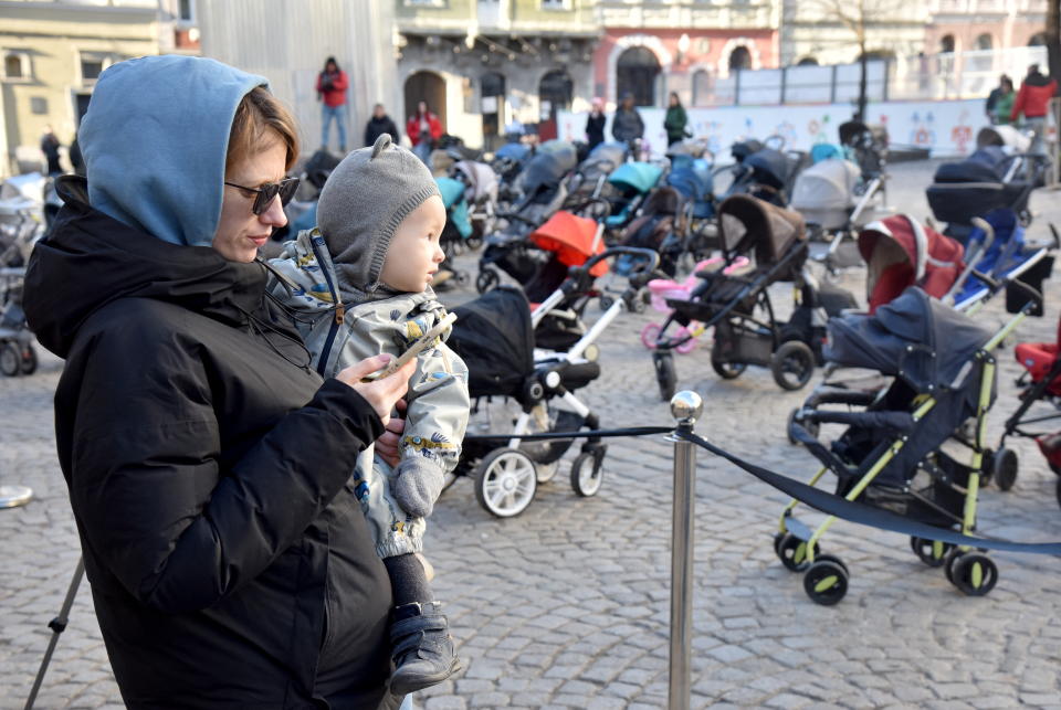 A woman holding a child walks past 109 empty prams placed in the center of Lviv during the 