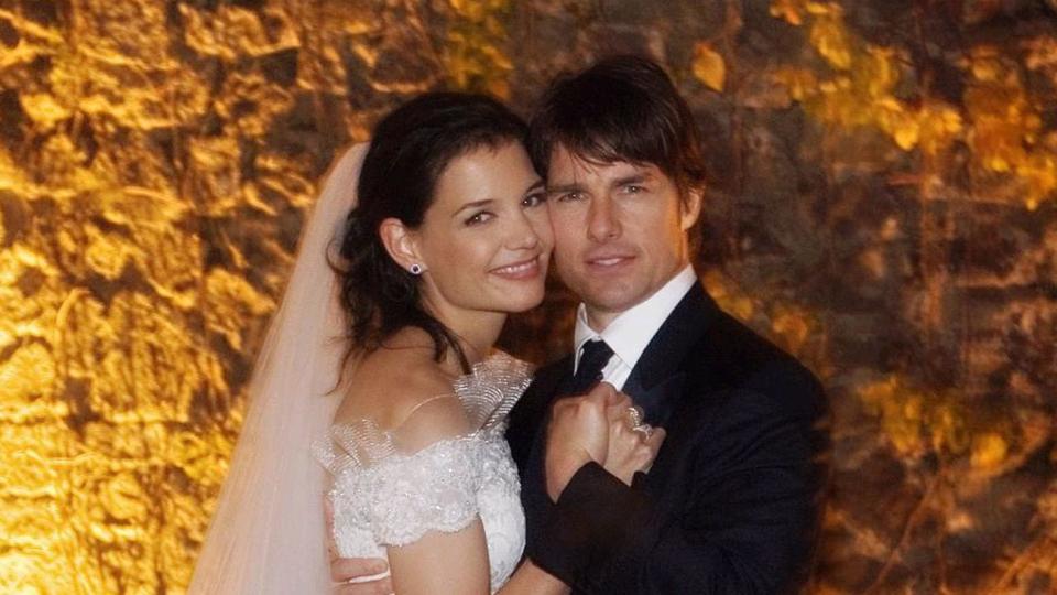 katie holmes and tom cruise smile for a wedding portrait while standing cheek to cheek, she wears a white off the shoulder gown with a veil, he wears a black suit