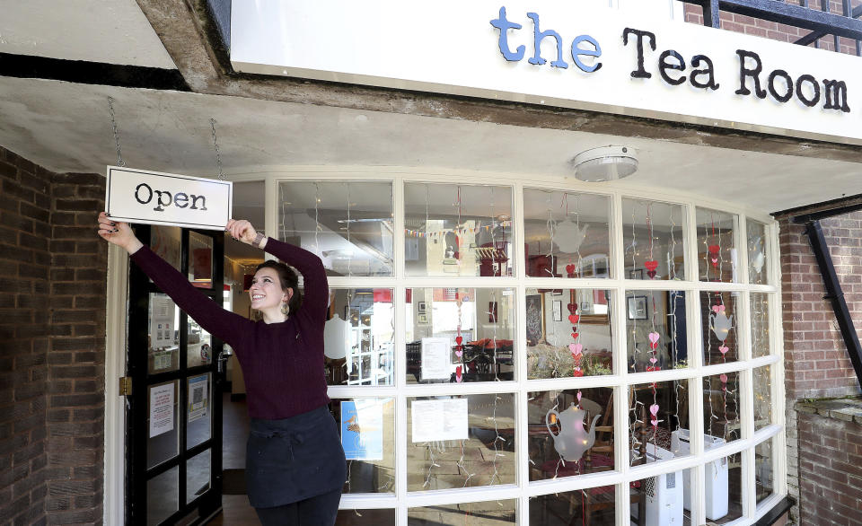 Harriet Henry, manager of The Tea Room in Knutsford, England, poses with the Open sign outside her cafe, as she prepares to open, Sunday April 11, 2021. Millions of people in Britain will get their first chance in months for haircuts, casual shopping and restaurant meals on Monday, as the government takes the next step on its lockdown-lifting roadmap. (Martin Rickett/PA via AP)