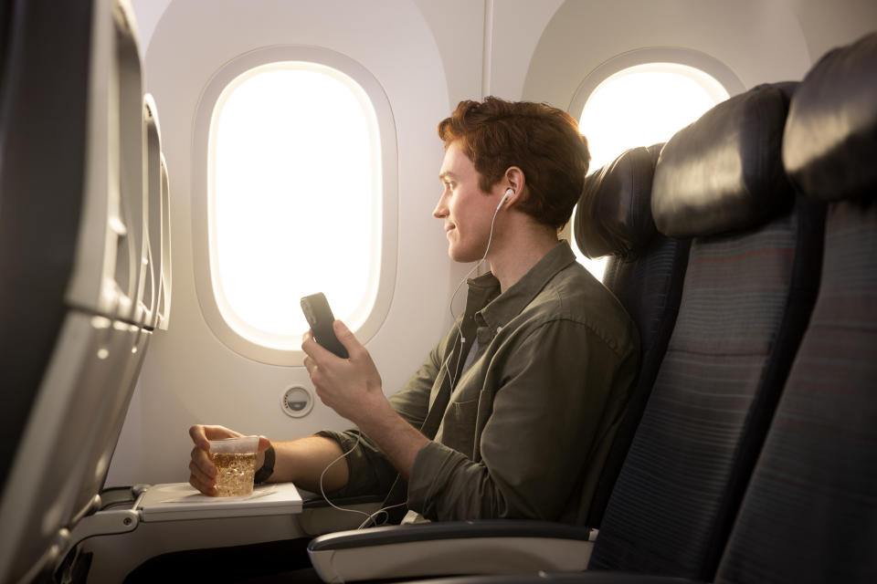 A man enjoys a soft drink while listening to headphones on an Air Canada flight