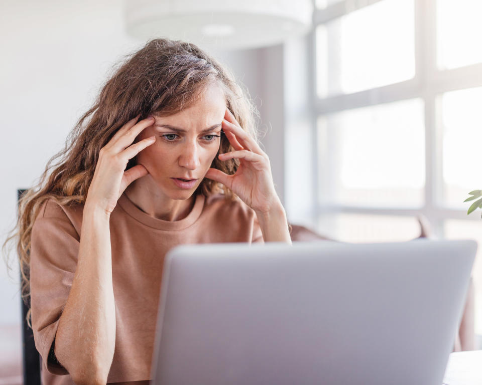 A woman at her laptop with her hands on her temples