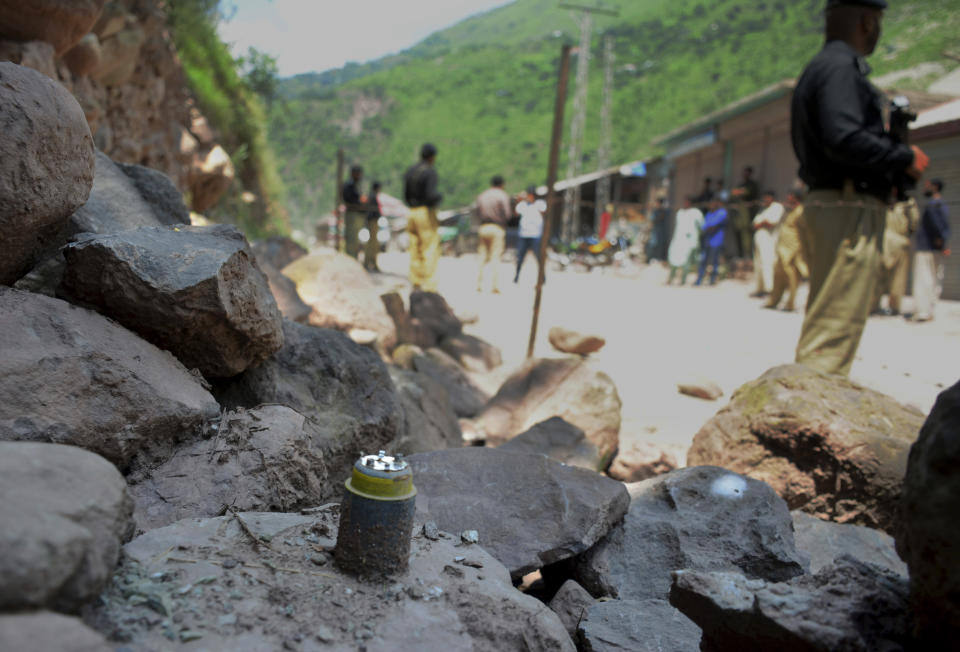 Police officers stand guard next to a munition fired by Indian forces on Nosehri village on the Line of Control that divides Kashmir between Pakistan India, near Muzaffarabad, Pakistan, Sunday, Aug. 4, 2019. Tensions have soared along the volatile, highly militarized frontier between India and Pakistan in the disputed Himalayan region of Kashmir, as India deployed more troops and ordered thousands of visitors out of the region. (AP Photo/M.D. Mughal)