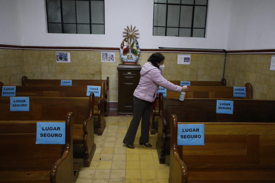 A parishioner sprays disinfectant on pews, marked with signs to encourage social distancing, ahead of Mass in a provisional chapel adjacent to the Nuestra Senora de Los Angeles, or Our Lady of Angels church, which is in the early stages of reconstruction three years after an earthquake collapsed almost half of its 18th-century cupola in Mexico City, Sunday, Oct. 4, 2020. The $2 million restoration effort here will take at least two years more; impatient residents often ask experts why it is taking so long. (AP Photo/Rebecca Blackwell)