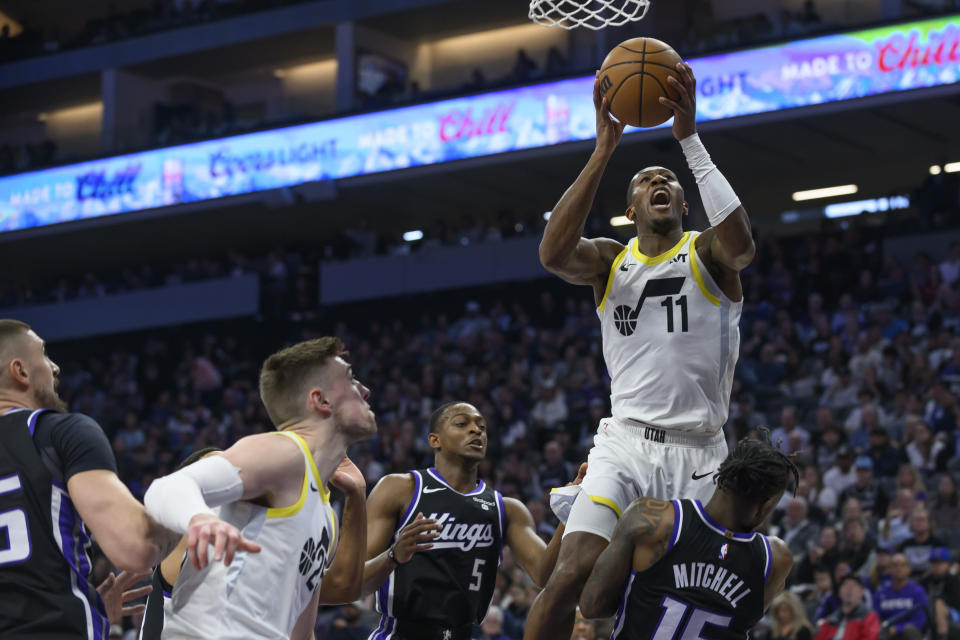 Utah Jazz guard Kris Dunn (11) drives to the basket over Sacramento Kings guard De'Aaron Fox (5) and guard Davion Mitchell during the first half of an NBA basketball game in Sacramento, Calif., Sunday, March 31, 2024. (AP Photo/Randall Benton)