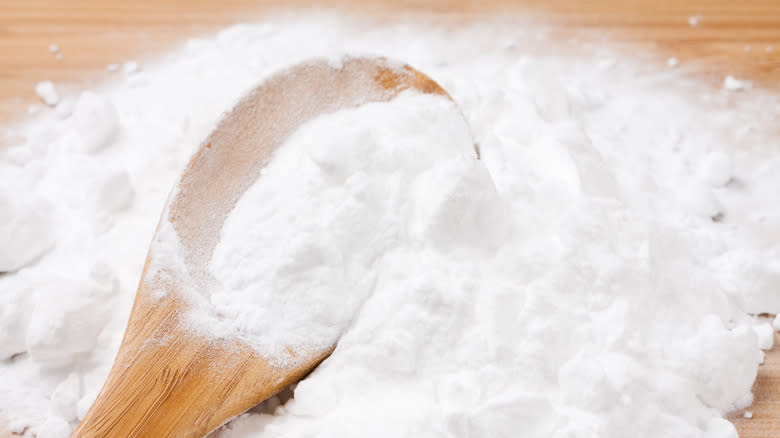 Closeup of a wooden spoon with baking soda on a wooden board