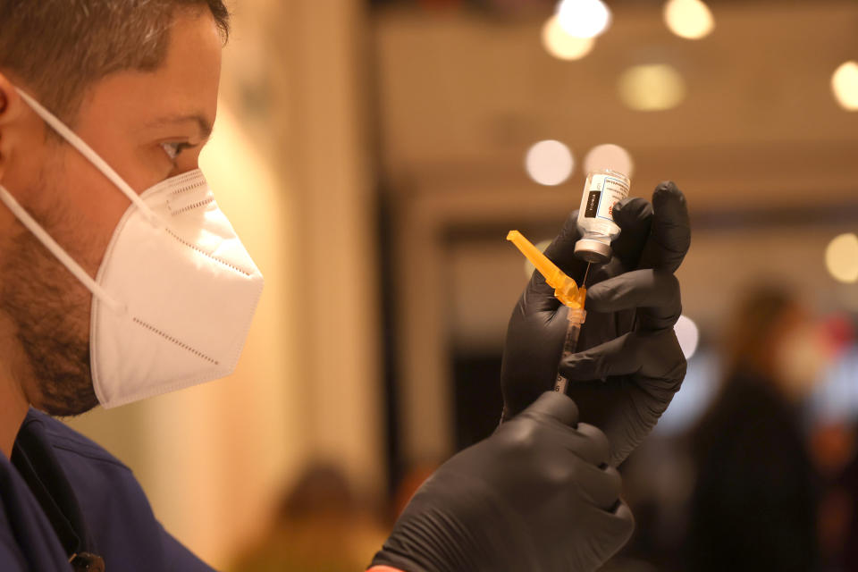 Jatniel Hernandez, in mask and black rubber gloves, fills a syringe with a COVID-19 vaccine booster shot.