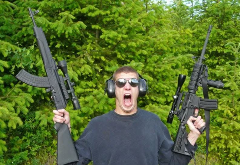 A man holding two assault-style rifles.