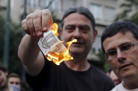 Anti-austerity protesters burn a euro note during a demonstration outside the European Union (EU) offices in Athens, Greece June 28, 2015. REUTERS/Alkis Konstantinidis
