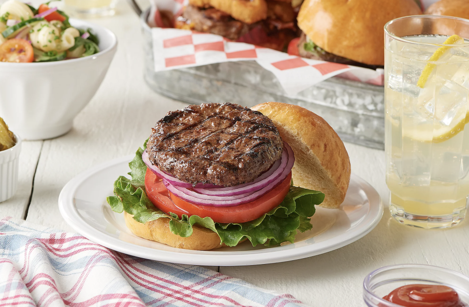 Burger on loaded bun with summer sides and drinks on table nearby